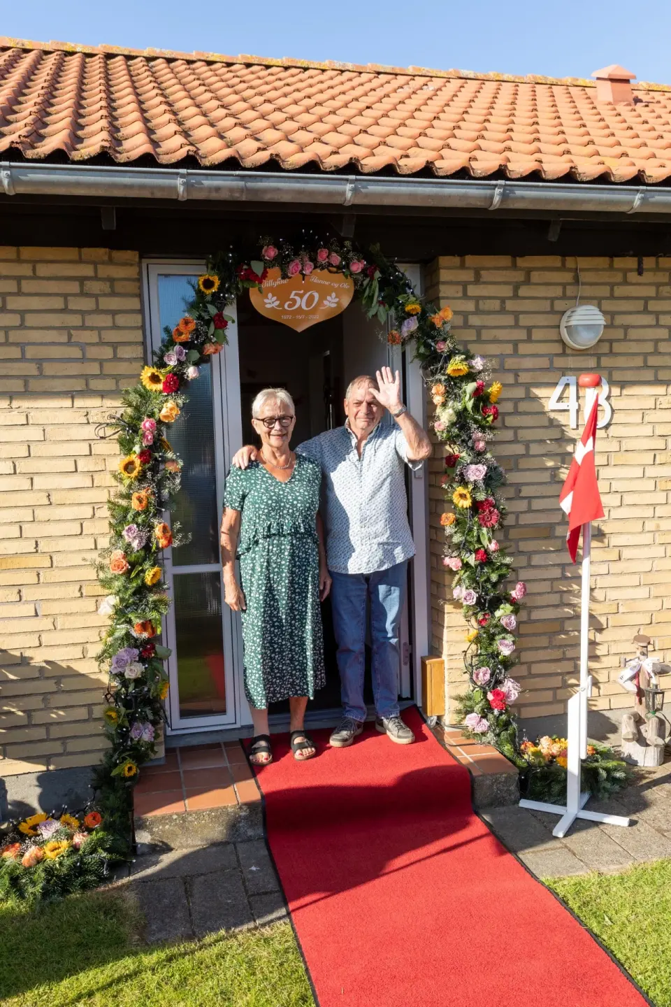 Jubilæumsparret under blomsterporten med dannebrog og rød løber